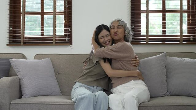 Cheerful asian people mature mom and young daughter hugging on sofa.