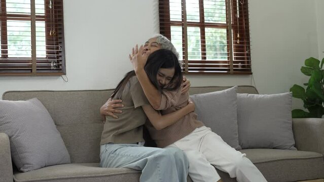 Cheerful asian people mature mom and young daughter hugging on sofa.