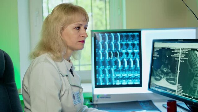 Blonde female doctor sitting in front of computer with patient's tomography picture. Focused medic typing the medical conclusion.