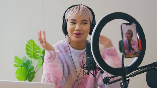 Female vlogger wearing headphones live streaming podcast looking on mobile phone - shot in slow motion