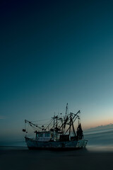 Tall lonely abandoned shrimp boat sitting on beach as the sun rises behind.