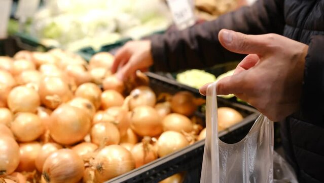 A man's hands choosing onion at the food market. Man take onion from thr stall in a food market. Man chosing vegetables in market