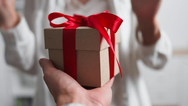 Presenting a gift to a loved one, giving a gift with a red ribbon, a gift box in the hands of a man, a festive day for a couple in love wedding anniversary valentine's day

