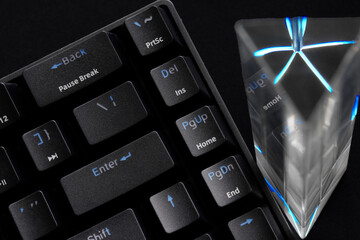 Fototapeta na wymiar Fragment of a trendy eSports computer keyboard and a glass prism on a dark background. copyspace. Macro. Selective focus.