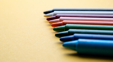 Set of crayons with different colors on a bright yellow background. Reference to children's play, abstract backgrounds and textures, coexistence between people and motor development.