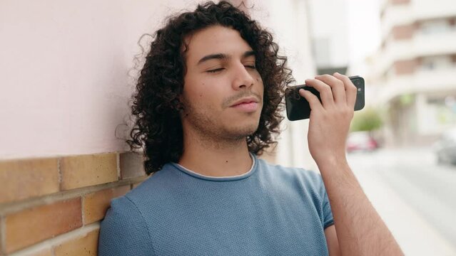Young latin man smiling confident listening audio message by the smartphone at street