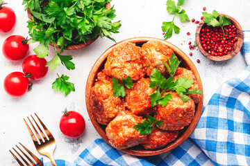 Meatballs in tomato sauce in wooden bowl on white kitchen table background, spices and herbs. Delicious home cooking. Top view