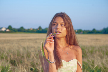 Fototapeta premium Stylish beautiful young girl in a fashionable dress walks around the field and poses, close-up portrait