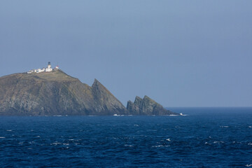 Cliffs and rocky coastline silhouette coast of Shetland Islands in Atlantic Ocean on sunny day with clouds, lighthouse and hills seen from cruiseship cruise ship liner with spray