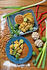 Flat lay photo of Batagor (fish cake), Indonesia's signature street food served with peanut sauce, plating in a wooden table. 