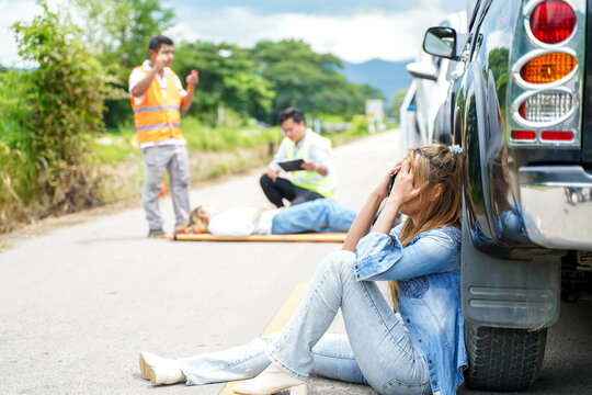 A young woman sits crying next to the car she crashed into someone on the road.