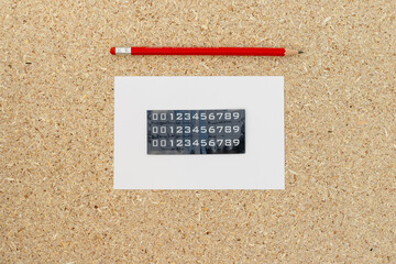 Sticker numbers on white post card with pencil on a cork board background