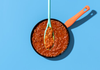 Bolognese sauce on a spoon above view on a blue background