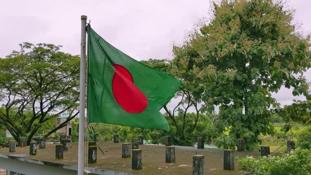 The official flag of Bangladesh is flying in the school playground. The national flying flag of Bangladesh in the cloudy sky.