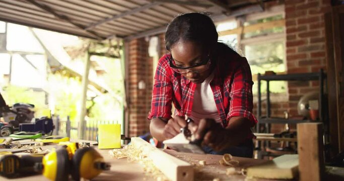 Profession, people, carpentry, woodwork - Female carpenter working with plane and wood plank at workshop