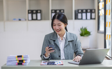 Smiling Asian business woman at work Using  phone and working on laptop sitting at her working place in office, copy space