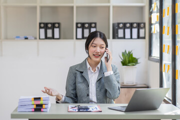 Smiling Asian business woman at work Call phone and working on laptop sitting at her working place in office, cheerful woman feel Excited and happy, copy space.