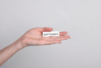 Woman's hand holds wooden white plate with inscription september on a gray background
