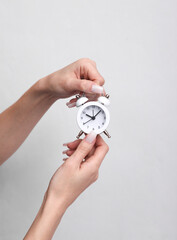 Woman's hand holding an alarm clock on gray background
