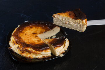 Basque cheesecake on a black slate, two pieces have been cut off and one is held high on a knife