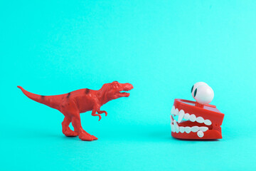 Toy red dinosaur tyrannosaurus rex with jumping teeth on a turquoise background. Minimalism creative layout