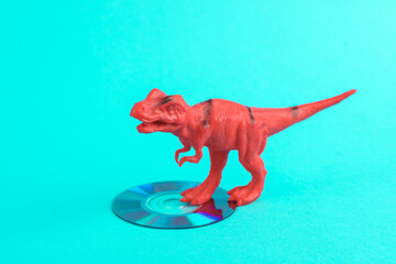 Toy red dinosaur tyrannosaurus rex with cd disk on a turquoise background. Minimalism creative layout