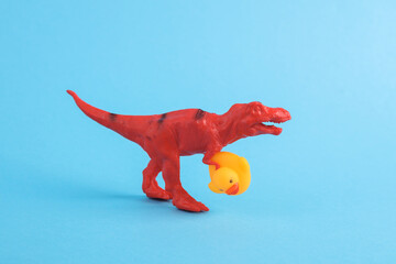 Toy red dinosaur tyrannosaurus rex with rubber duck on a turquoise background. Minimalism creative...