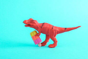 Toy red dinosaur tyrannosaurus rex with ice cream on a turquoise background. Minimalism creative...