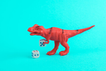 Toy red dinosaur tyrannosaurus rex with dice on a turquoise background. Minimalism creative layout