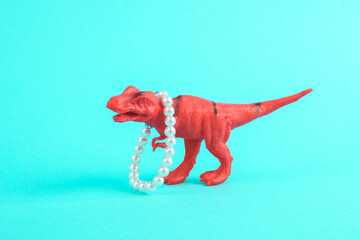 Toy red dinosaur tyrannosaurus rex with pearls necklace on a turquoise background. Minimalism...