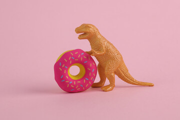 Toy dinosaur tyrannosaurus rex with donut on pink background. Minimalism creative layout