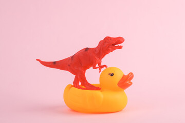 Toy red dinosaur tyrannosaurus rex with rubber duck on pink background. Minimalism creative layout