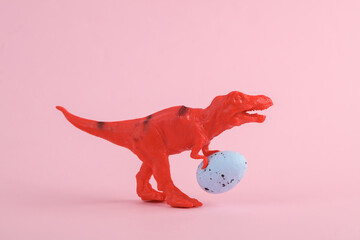 Toy red dinosaur tyrannosaurus rex with easter egg on pink background. Minimalism creative layout