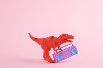Toy red dinosaur tyrannosaurus rex with boombox audio player on pink background. Minimalism...