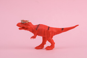 Toy dinosaur tyrannosaurus rex with crown on pink background. Minimalism creative layout
