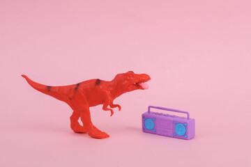 Toy red dinosaur tyrannosaurus rex with boombox audio player and headphones on pink background. Minimalism creative layout