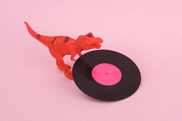 Toy dinosaur tyrannosaurus rex with vinyl plate on pink background. Minimalism creative layout