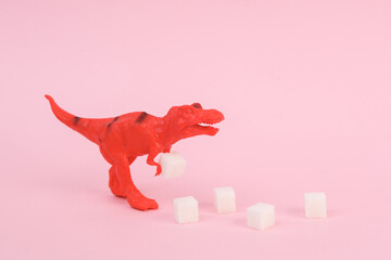 Toy dinosaur tyrannosaurus rex with sugar cubes on pink background. Minimalism creative layout