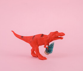 Toy dinosaur tyrannosaurus rex with christmas tree on pink background. Minimalism creative layout