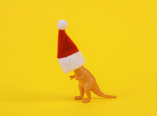 Toy dinosaur with santa hat on yellow background. Creative Christmas layout