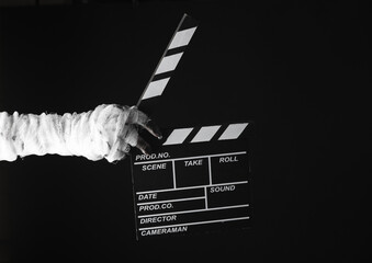 Mummy's hand wrapped in bandage holds movie clapperboard isolated on black background. Halloween,...