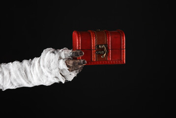 Mummy hand holding pirate chest isolated on black background. Halloween concept