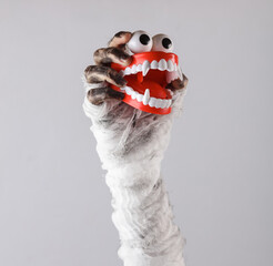 Mummy's hand wrapped in bandage holds monster joke jaw isolated on gray background. Halloween concept
