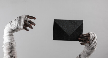 Mummy hand holding black envelope isolated on gray background. Halloween concept