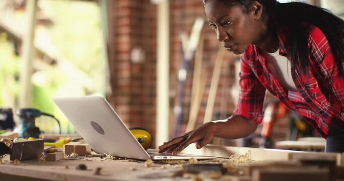 African American female carpenter working with computer laptop in workshop