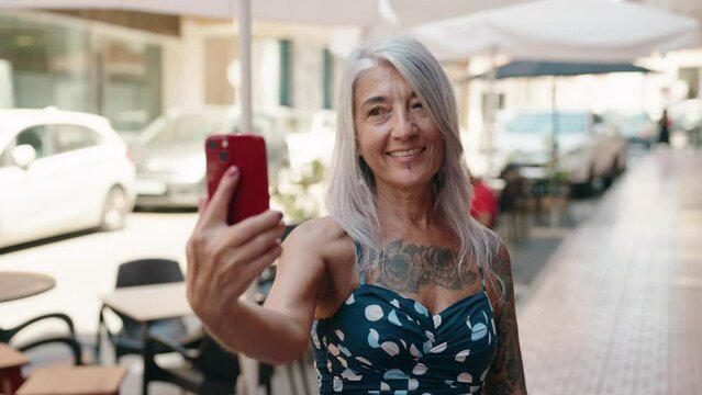 Middle age grey-haired woman smiling confident making selfie by the smartphone at street
