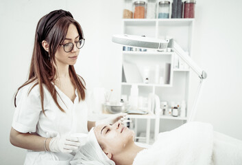Cosmetological procedures. Beauty salon, doctor in gloves touching face of beautiful woman with closed eyes with brush.