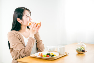 朝食で美味しそうに笑顔でトーストされた食パンを食べる日本人女性
