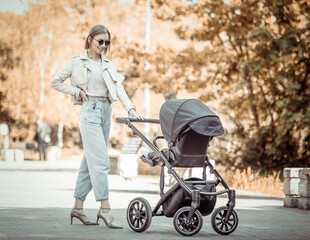 Obraz premium Young stylish mom in sunglasses walking with stroller in the park