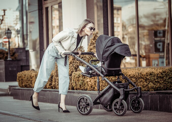 Stylish loving mom walks with a stroller in the city location. Maternity, lifestyle